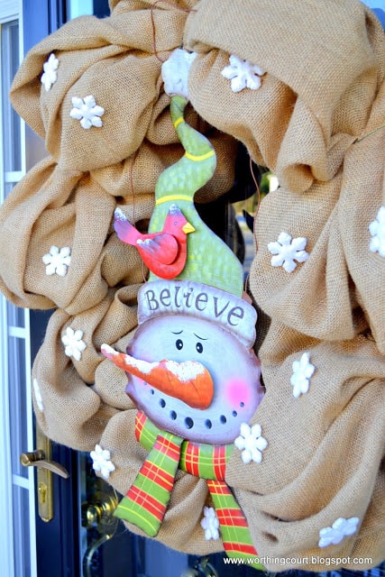 A burlap wreath with a tin snowman on a winter front porch