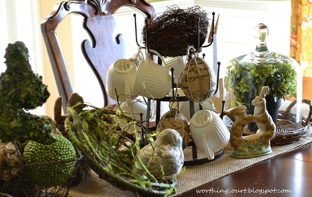 A faux bird nest and bird flank a mug tree filled with burlap eggs and vintage Easter images add lots of interest to this Easter centerpiece.