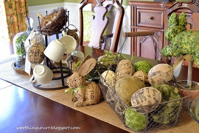 A wire basket filled with burlap eggs and orbs covered with natural elements add a lot of texture to this Easter centerpiece.