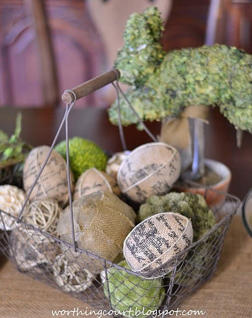 An Easter centerpiece with an aged wire basket filled with burlap eggs and a variety of decorative orbs