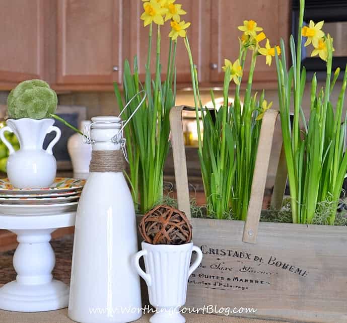 The yellow daffodils in a wooden container beside white vases.