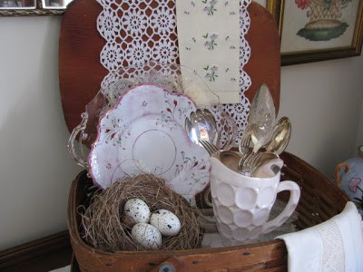 A little basket with a birds nest and a white coffee mug with cutlers and a decorative plate.