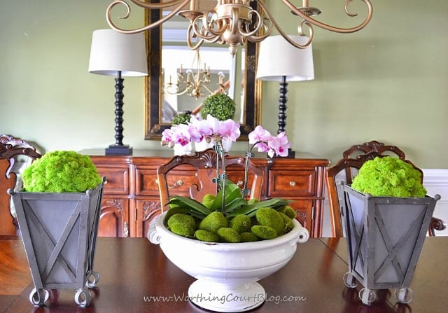 Styrofoam balls covered with reindeer moss and placed in zinc planters flank an orchid filled urn as part of spring decor in a dining room