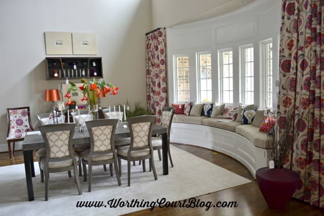 Curved window with a bench filled with multiple pillows that pull together all of the colors used in the house