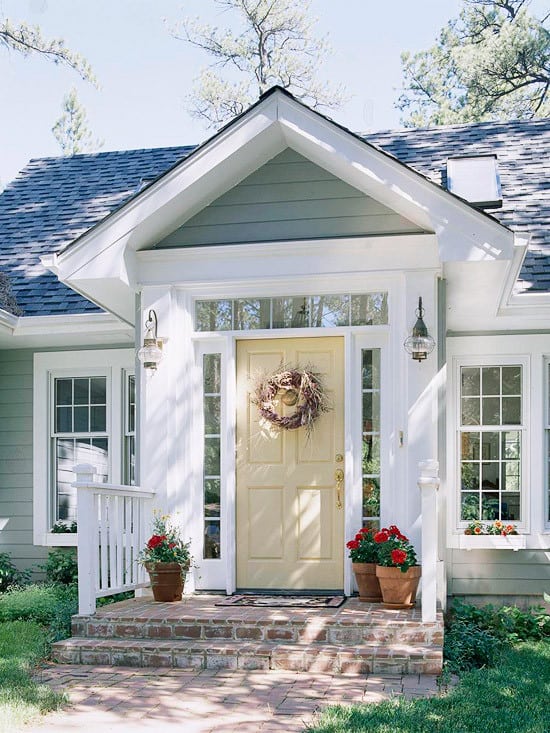 A neutral pale yellow door with red flowers on the porch.