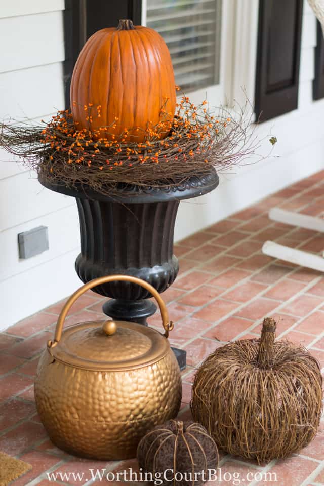 The large urn with a pumpkin on top of it.   A copper pot is beside the urn as well as two other decorative pumpkins.
