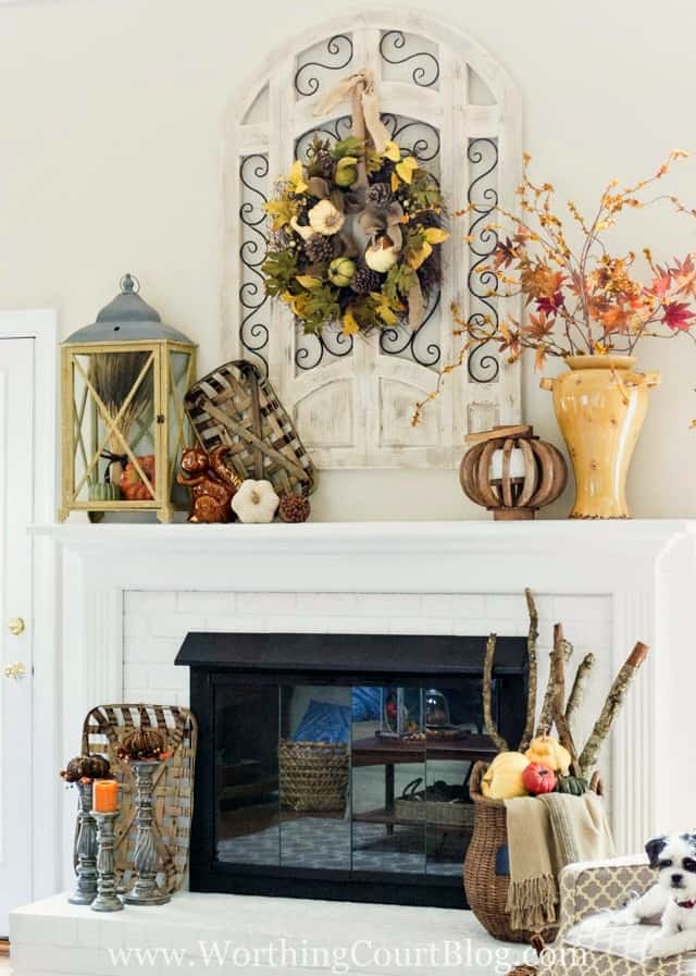 The sitting room fully decorated for fall with a fall wreath, an urn filled with leaves and candlesticks with twig pumpkins.