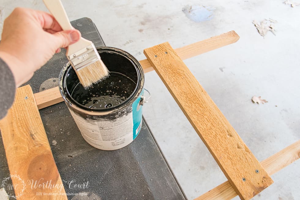 A can of black paint and a paint brush dipped into it.