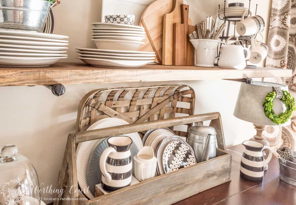 A vintage looking wood toolbox filled with white, gray and black plates looks right at home on the sideboard of a farmhouse style breakfast area and rustic shelf vignette.