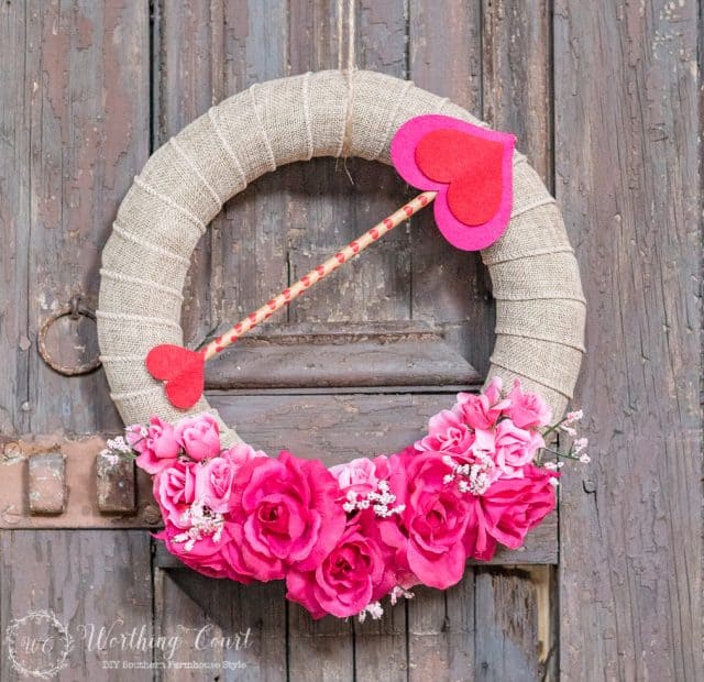 A jute wreath with pink flowers a pink love arrow.