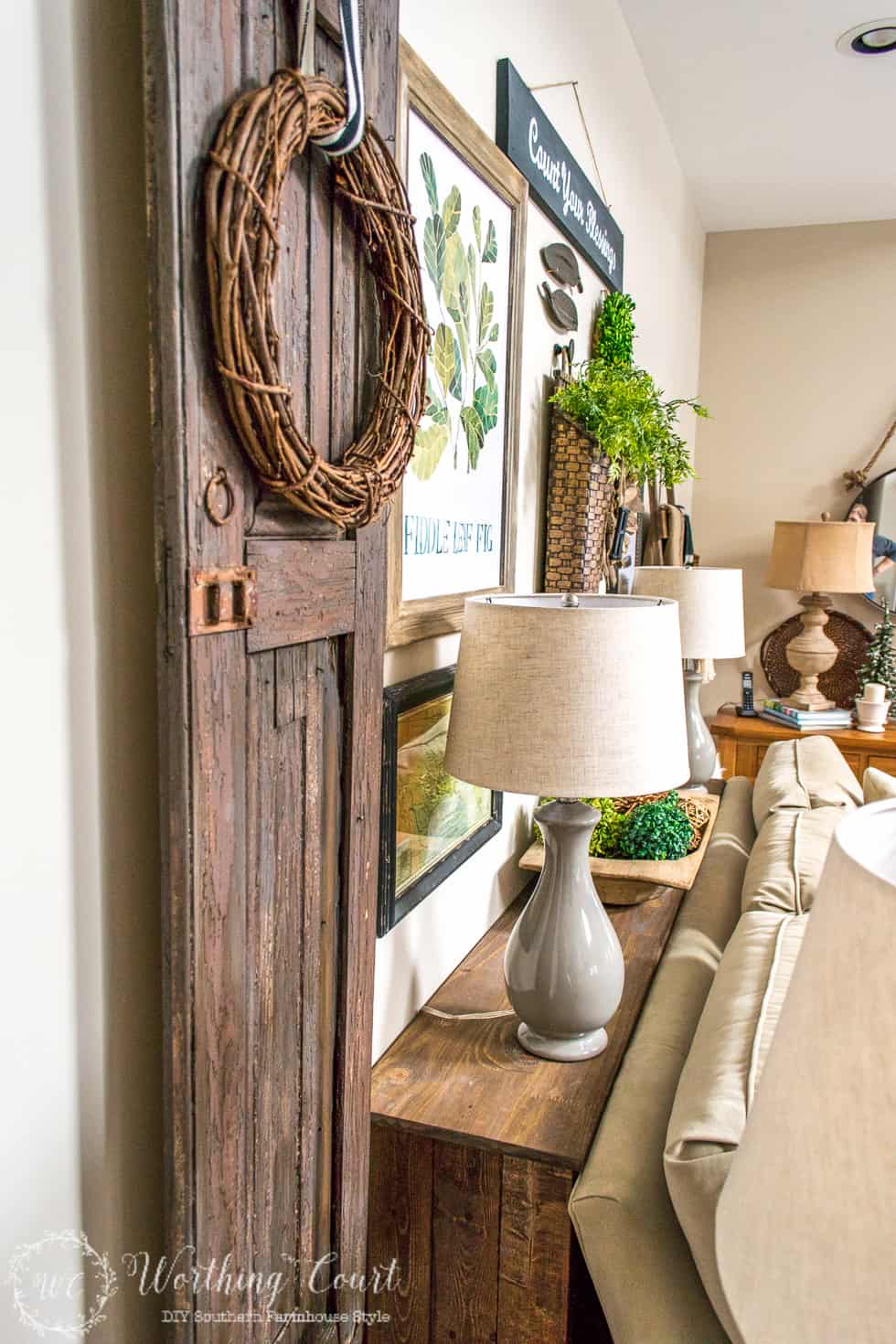 The rustic sofa table with a barn door beside it and a small grey lamp on it.