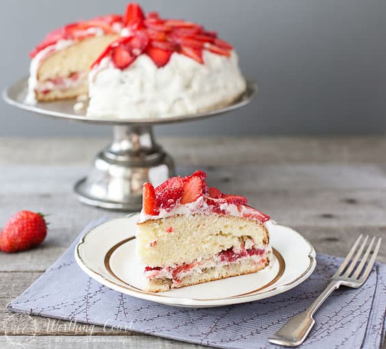 There is a strawberry cake on a cake stand and a piece of the cake on a plate.