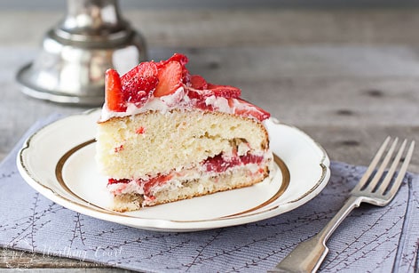 Strawberry cake on a white plate with a fork beside it.