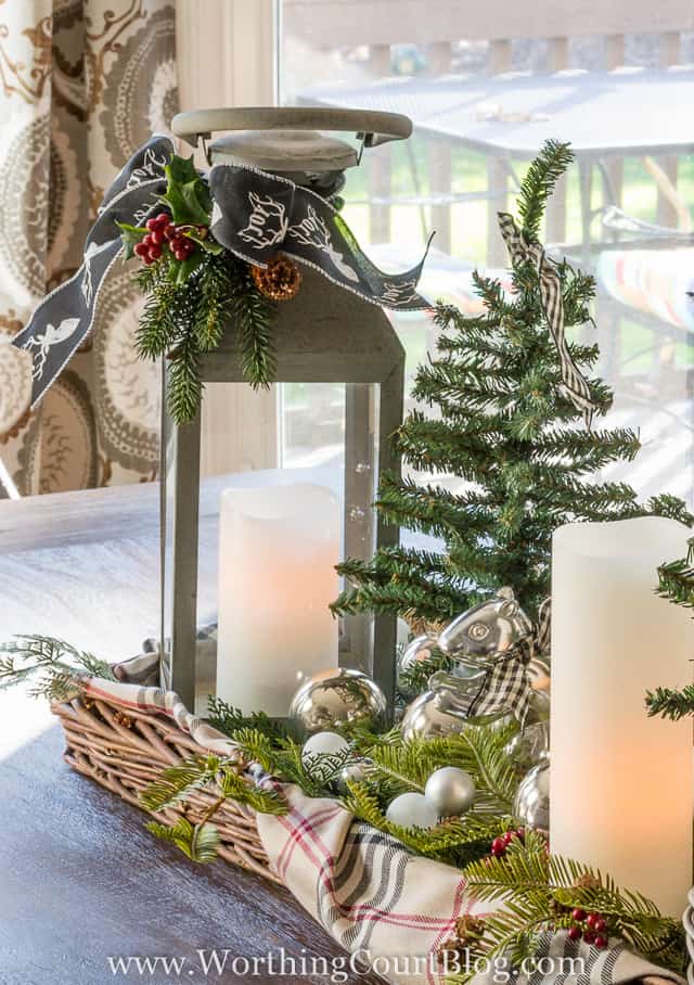 Christmas centerpiece in a wicker tray with lanterns, candles and mini tree.