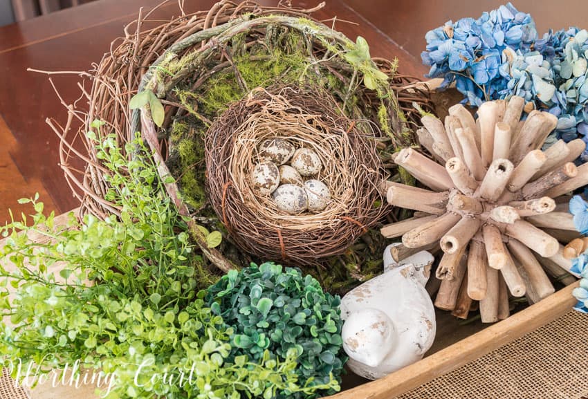 Wood dough bowl filled with spring decor such a small birds nest with faux eggs.
