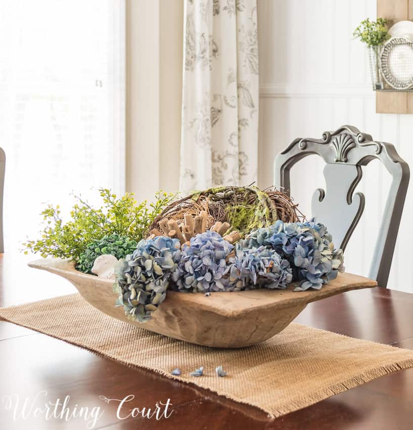 Large wooden dough bowl centerpiece filled with spring decor on the dining room table.