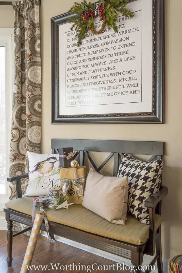 A small sitting bench with farmhouse pillows and a wreath on a picture frame above on the wall.