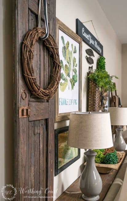 A rustic farmhouse texture filled gallery wall with a door on the wall and twig wreath on it.