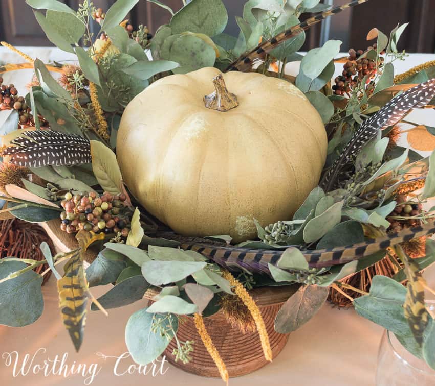 Thanksgiving centerpiece in a wooden pedestal bowl using a faux pumpkin, eucalyptus leaves and feathers || Worthing Court