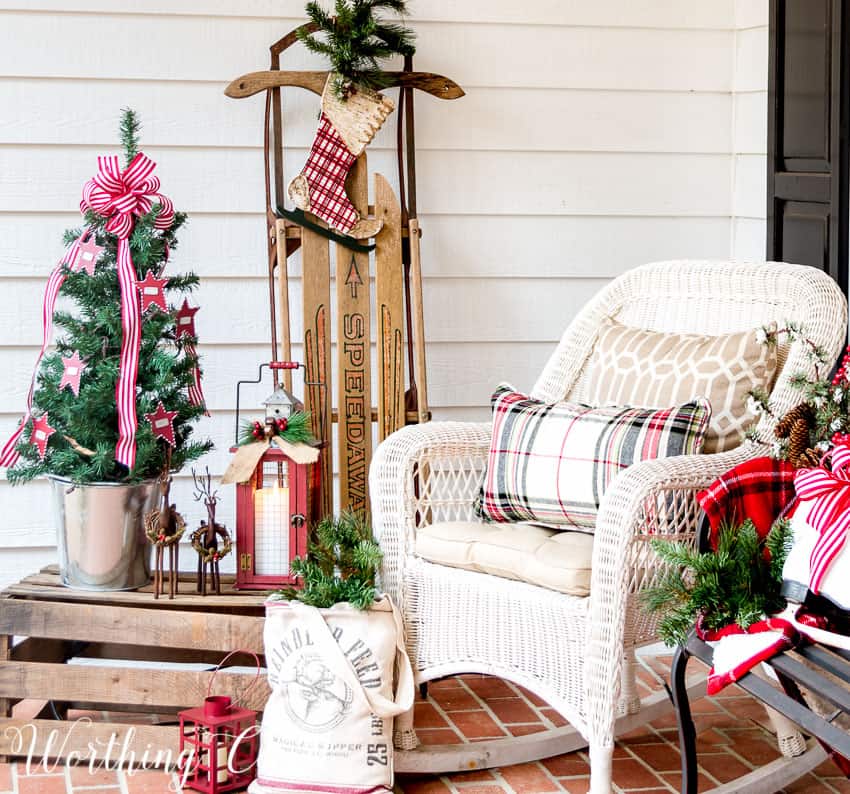 There is a white wicker rocking chair with a plaid pillow on the front porch.