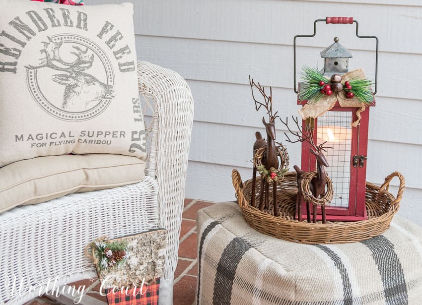 A white neutral reindeer pillow is on the wicker white chair.