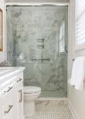 bathroom with marble-look tile shower and a white vanity