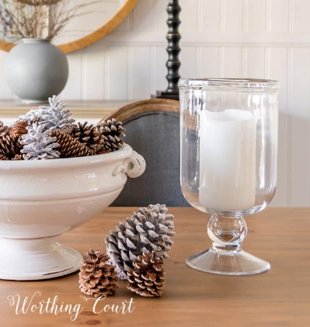 bowl filled with pinecones beside a large glass candleholder