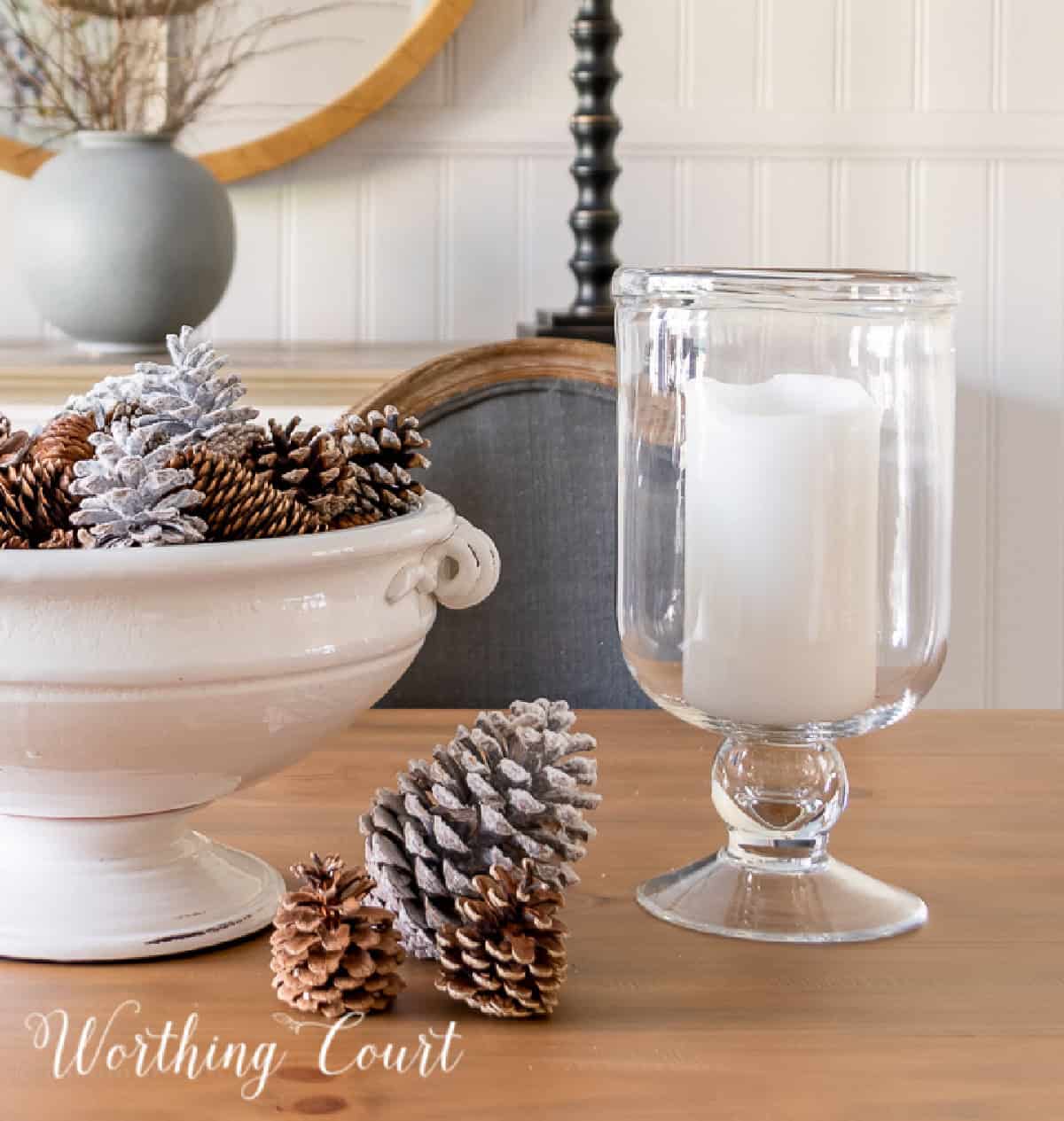 bowl filled with pinecones beside a large glass candleholder