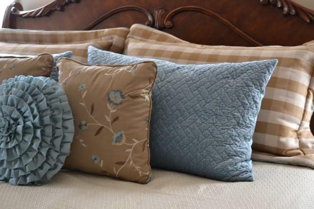 an assortment of blue and cream throw pillows on a bed against a wood headboard