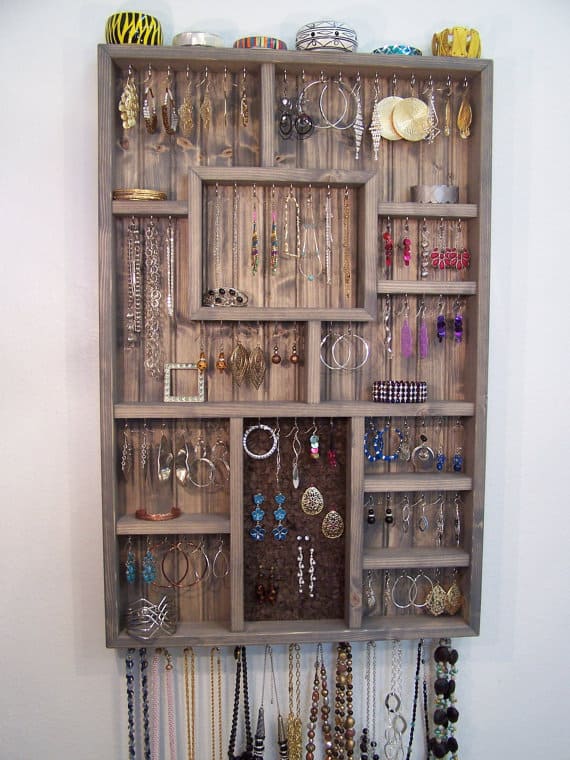 A wooden jewellery organizer on the wall in the bedroom.