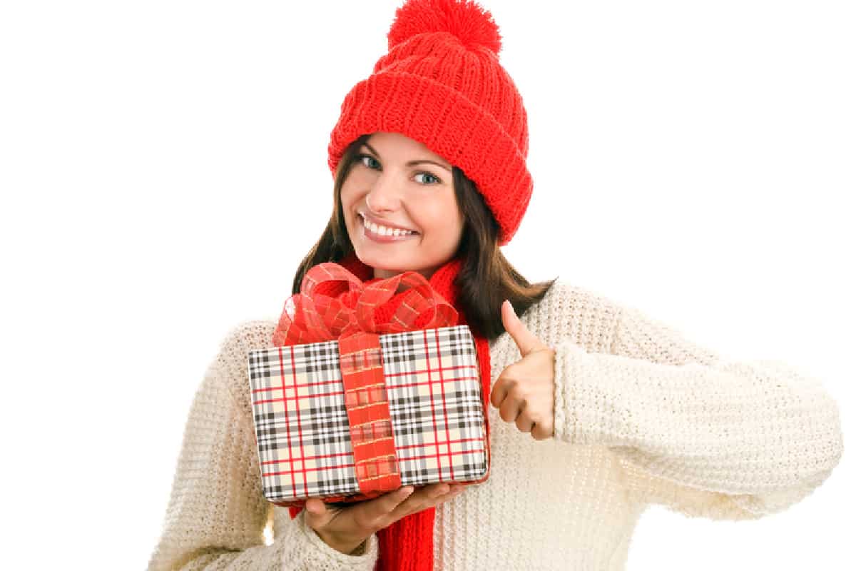 girls in a white sweater and red hat holding a wrapped gift