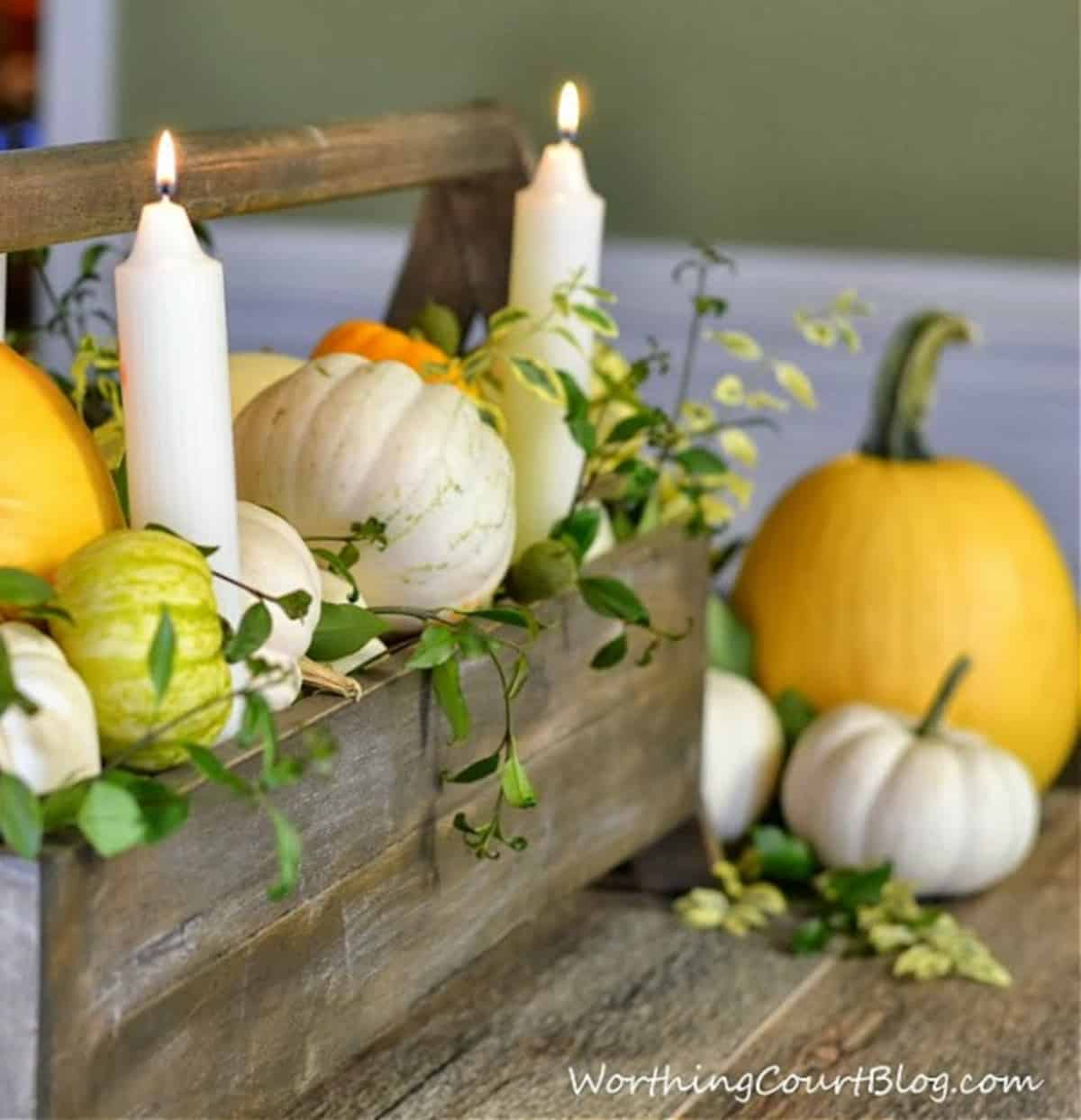 long gray wood tool box filled with yellow and white pumpkins, white candles and sprigs of greenery for a Thanksgiving centerpiece