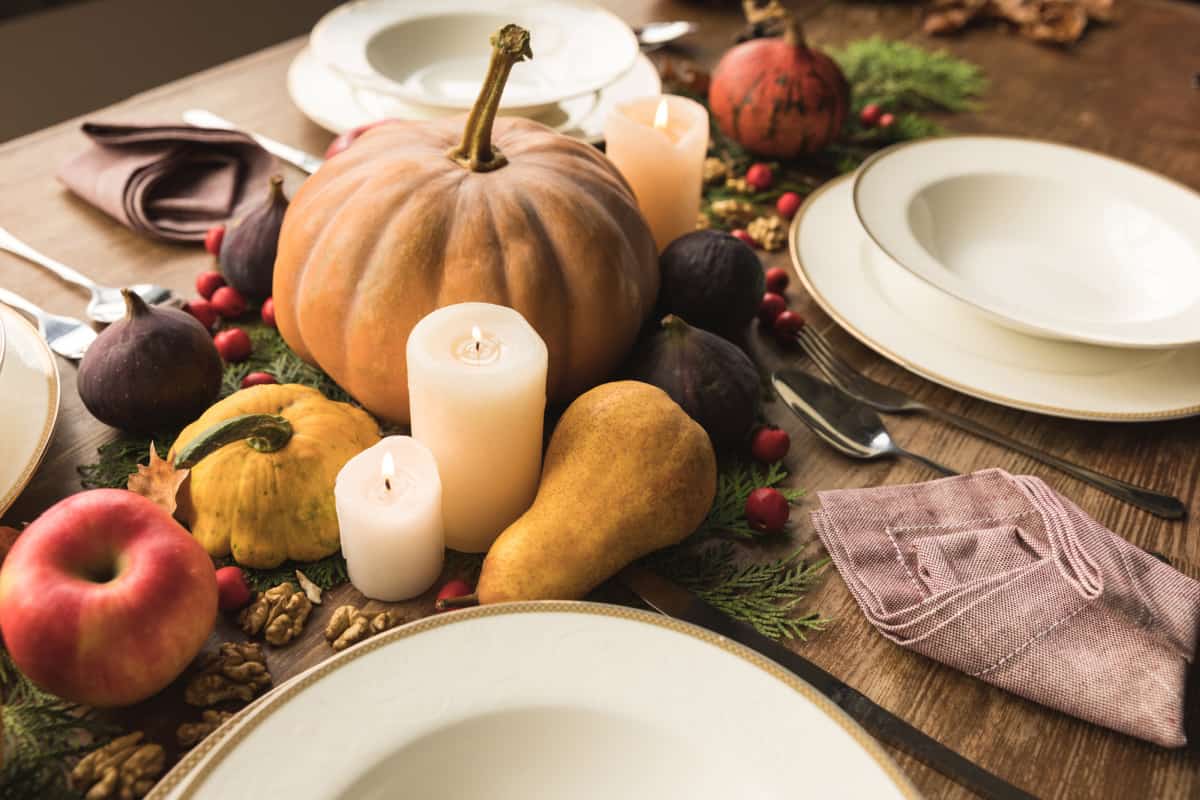 diy Thanksgiving centerpiece with pumpkins, gourds, foliage and candles in the middle of white plate place settings