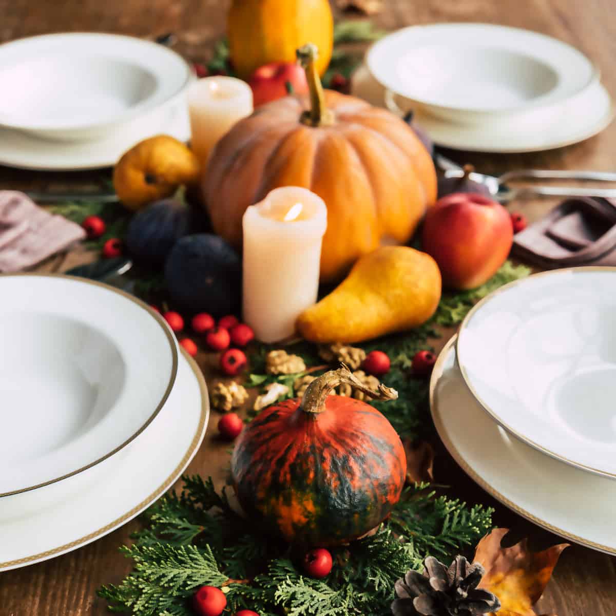 diy Thanksgiving centerpiece with pumpkins, gourds, foliage and candles in the middle of white plate place settings