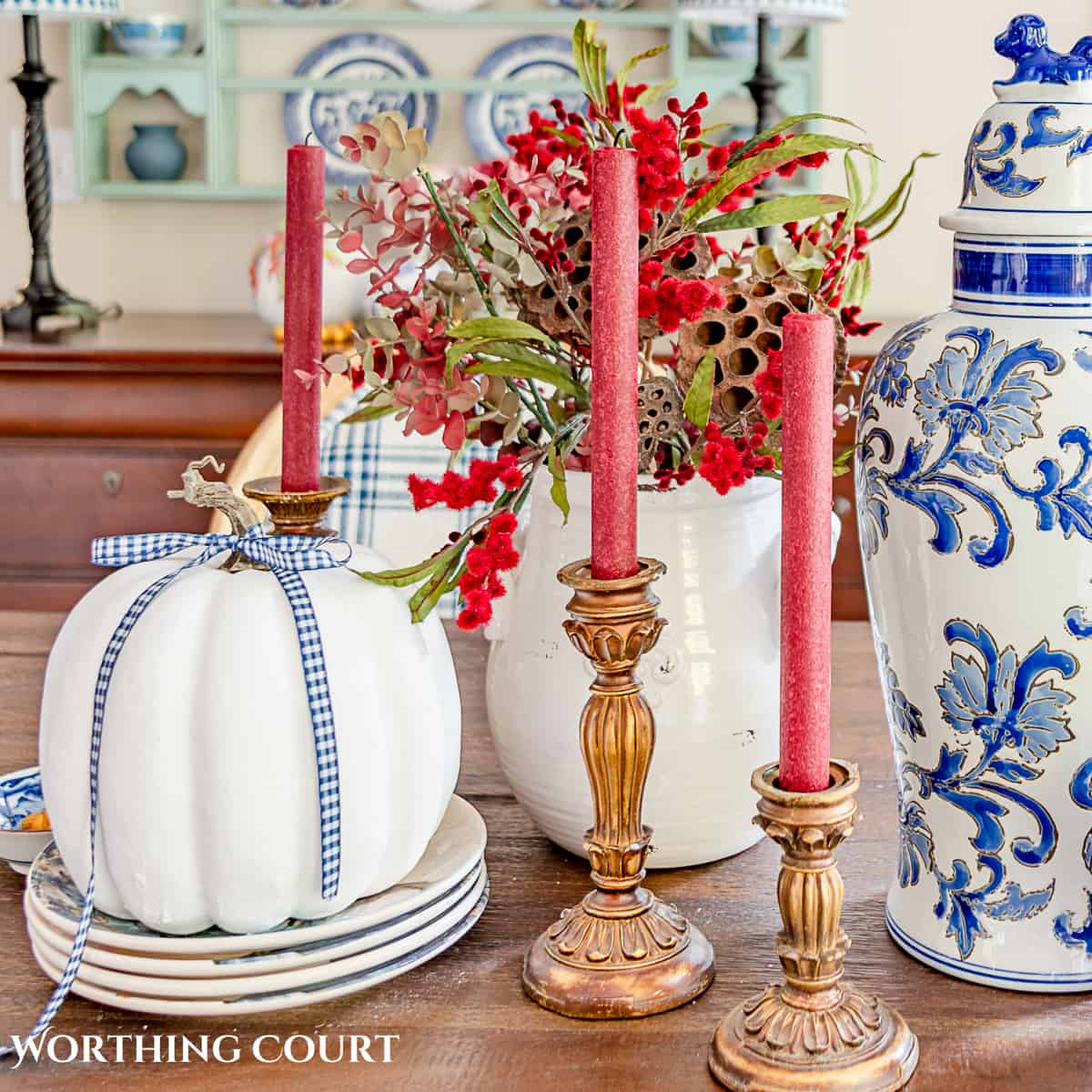 fall centerpiece using blue and white accessories, a white pumpkin, fall colored florals and burgundy candles in gold candle holders