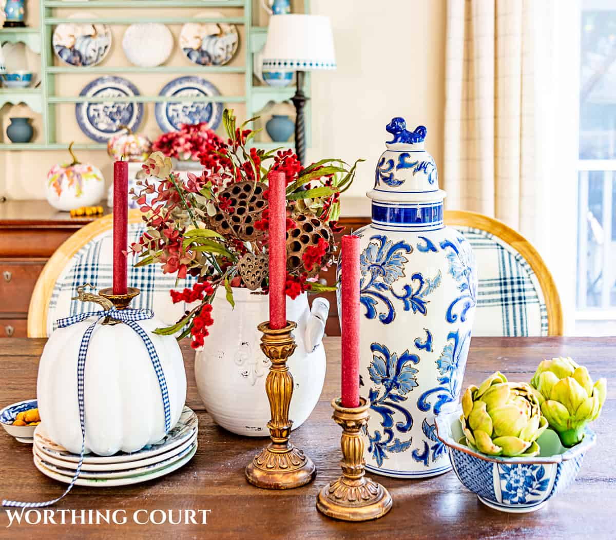 fall centerpiece using blue and white accessories, a white pumpkin, fall colored florals and burgundy candles in gold candle holders