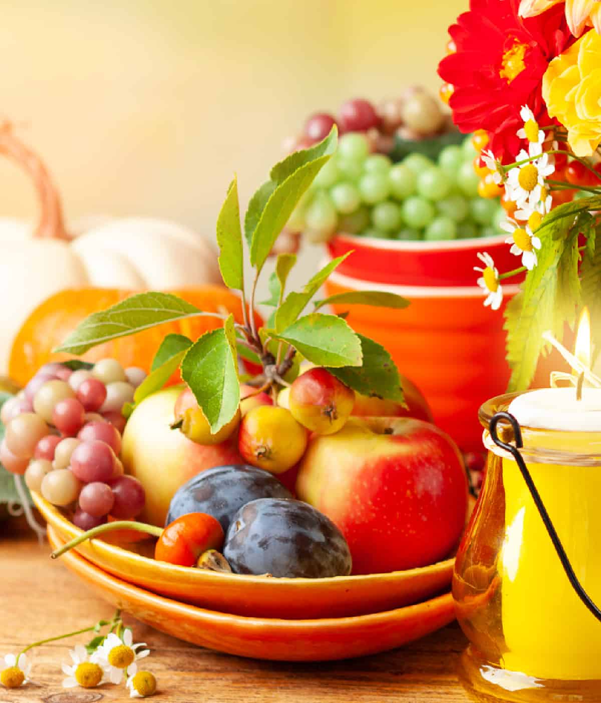 stack of orange plates with arrangement of different fall fruits beside a votive candle