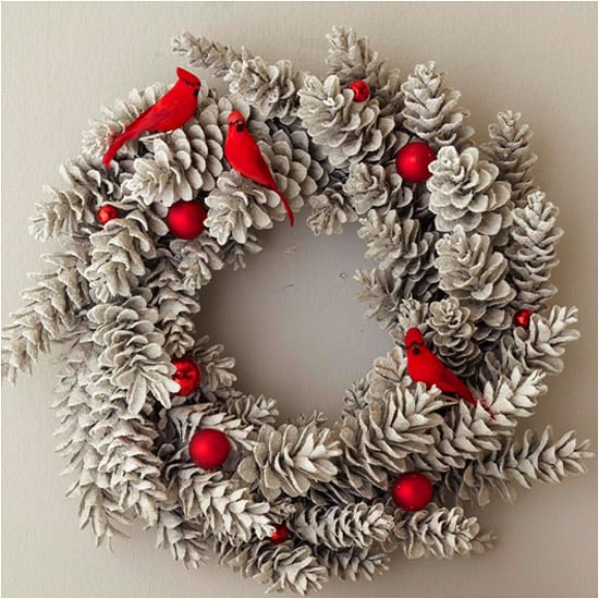 Flocked pine cone wreath with red birds and red ornaments on it.