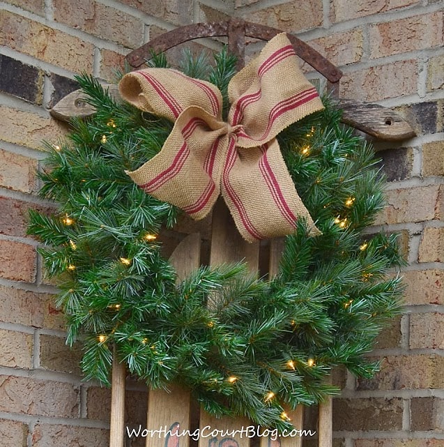 Christmas wreath attached to a vintage sled with a ribbon made from upholstery strapping attached.