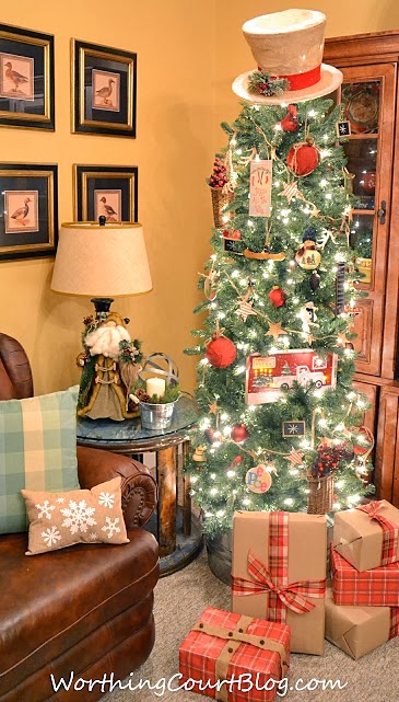 A tall Christmas tree in the corner of the room with red ticking garland.