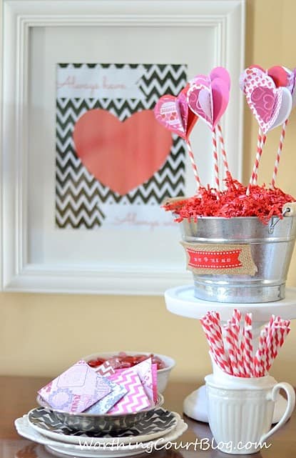 A plate with pink napkins, and a bucket filled with pink and white hearts.