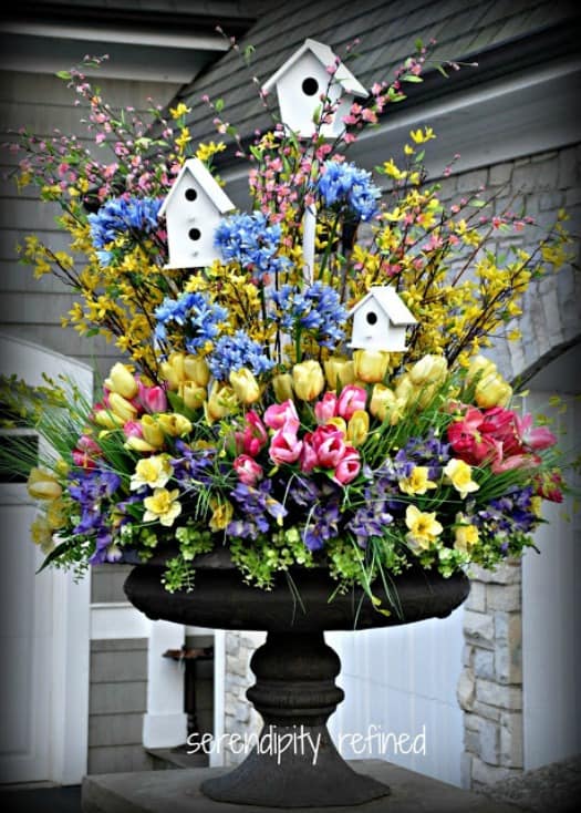 A stunning urn filled with a variety of spring flowers, greenery and birdhouses.