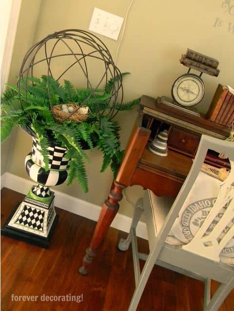 A fern topiary beside a wooden desk.