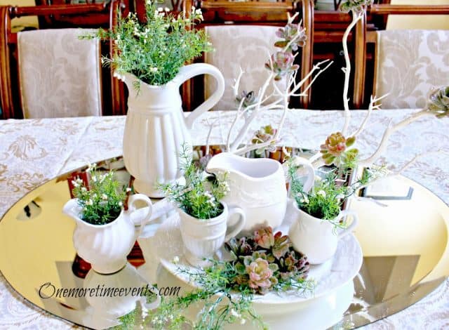 A small mirror tray with white dishes with plants in them.