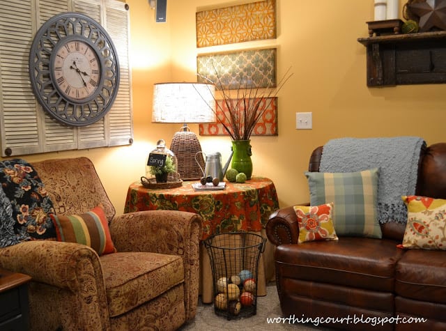 A family room with a large clock on the wall and bright pillows on the couches.