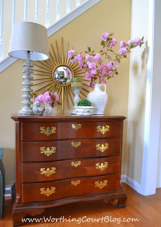 A wooden dresser with purple flowers in vases on top.