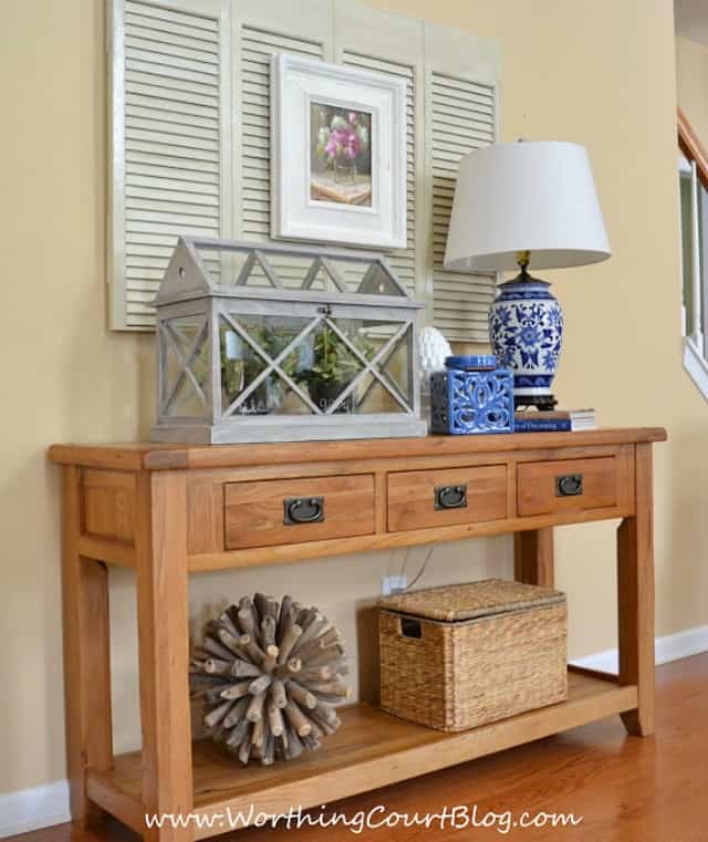 A wooden hallway console table with a lamp and terrarium on it.