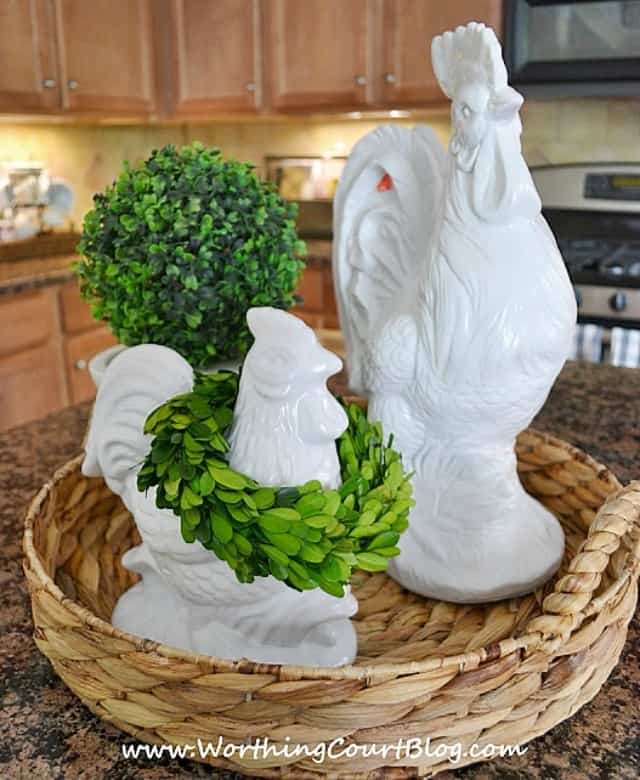 Two white porcelain roosters one with a green wreath around its neck on the table.
