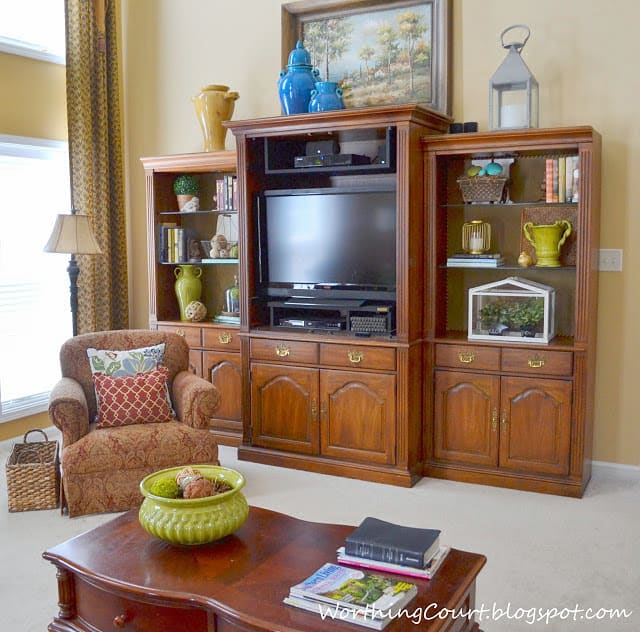 There is a wooden entertainment center in the living and a green bowl on the table.