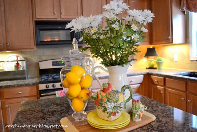 There are flowers in a vase, a clear glass vase with oranges in them on the kitchen island.